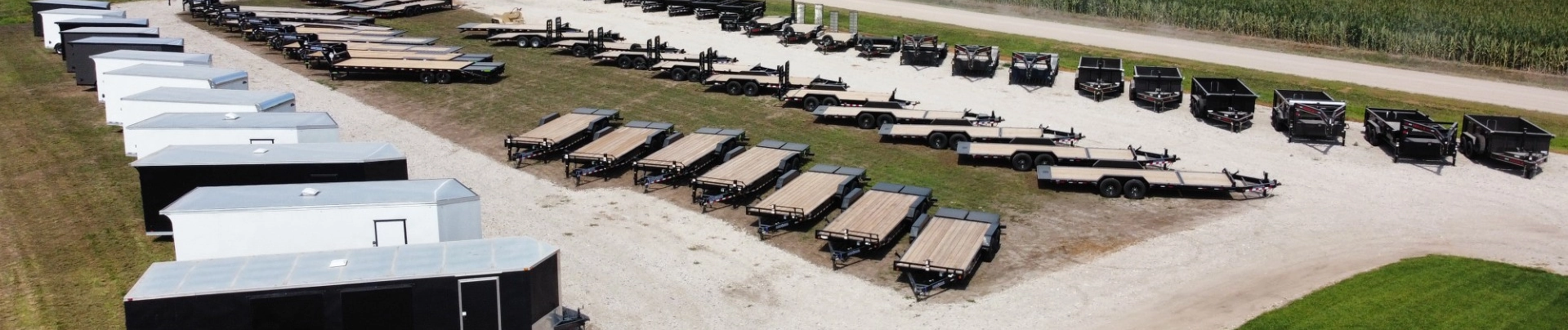 Rows of enclosed and flatbed trailers displayed in an open lot near a rural road.