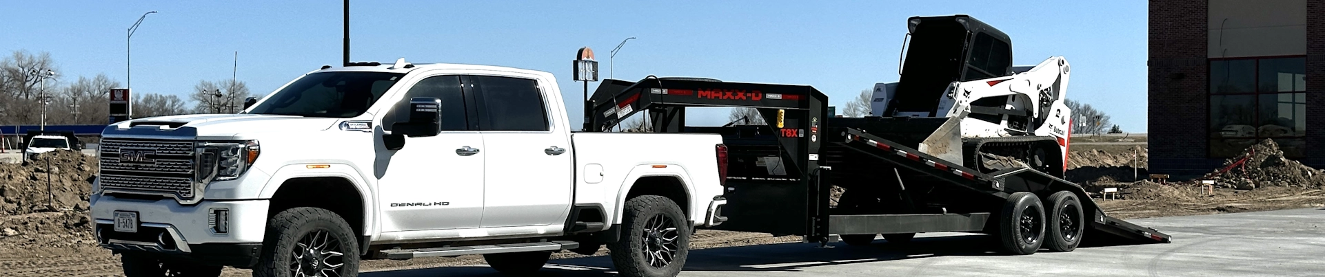 White GMC truck towing a trailer with a skid steer loader