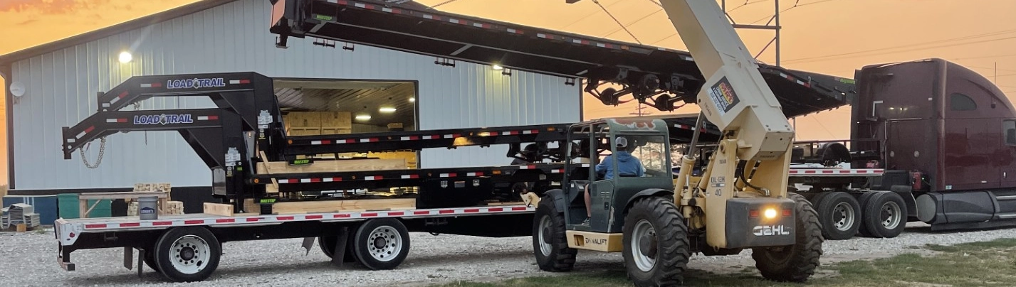 Forklift loading a stack of Load Trail gooseneck trailers onto a flatbed truck.